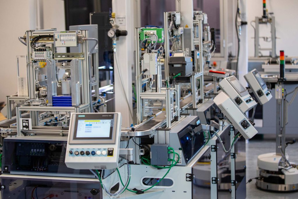 Industrial machinery in a manufacturing setting. A screen is nearest to us with multiple buttons on a control panel